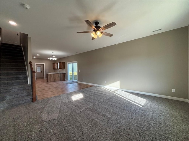 unfurnished living room with dark colored carpet and ceiling fan with notable chandelier