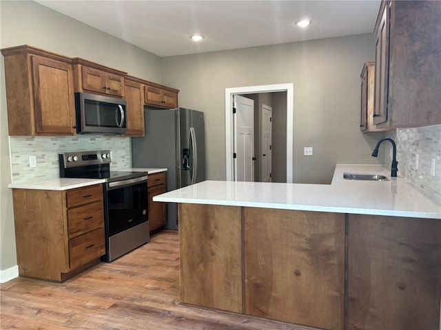 kitchen featuring kitchen peninsula, light wood-type flooring, tasteful backsplash, stainless steel appliances, and sink