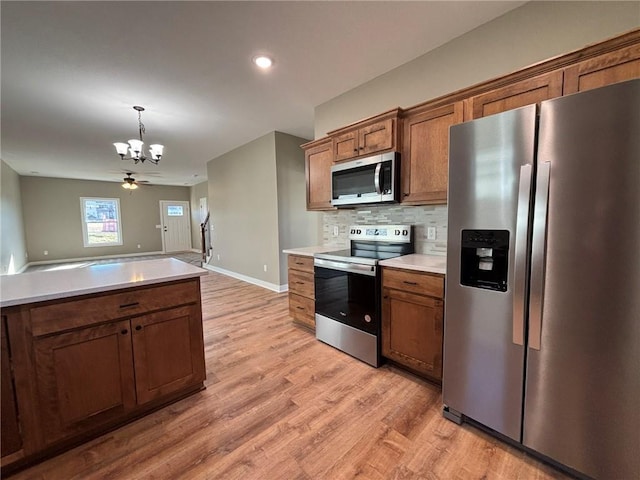 kitchen with decorative backsplash, appliances with stainless steel finishes, ceiling fan with notable chandelier, decorative light fixtures, and light hardwood / wood-style flooring