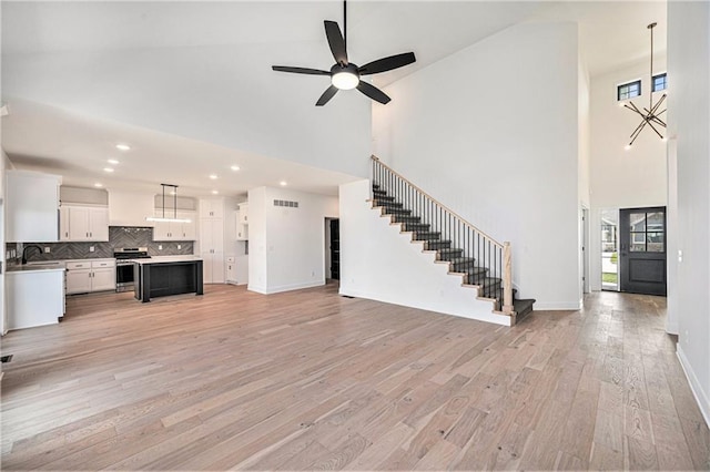 unfurnished living room with high vaulted ceiling, sink, light wood-type flooring, and ceiling fan