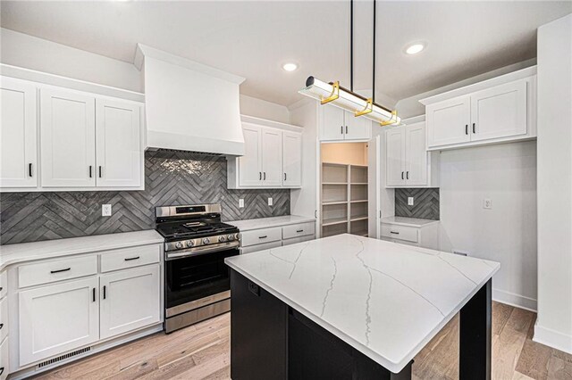 kitchen with a kitchen island, white cabinetry, stainless steel range with gas cooktop, pendant lighting, and light hardwood / wood-style flooring