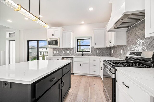 kitchen with white cabinetry, appliances with stainless steel finishes, custom exhaust hood, and hanging light fixtures