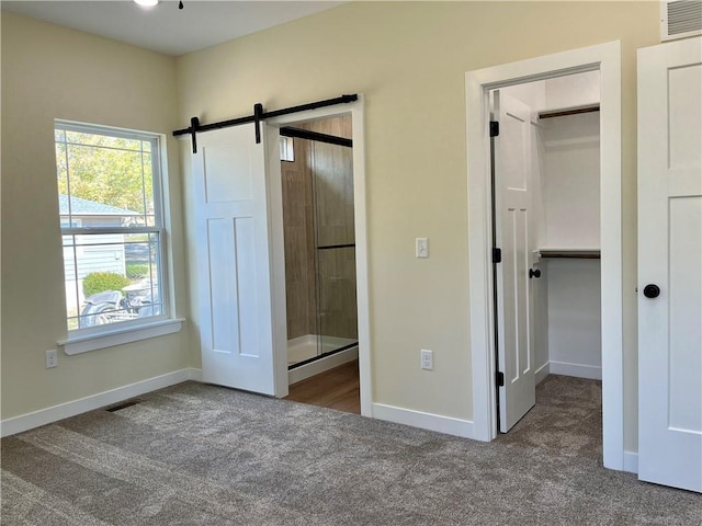 unfurnished bedroom featuring a barn door, carpet flooring, and visible vents