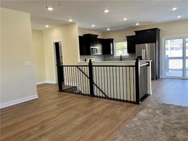 kitchen featuring tasteful backsplash, stainless steel appliances, dark cabinetry, and wood finished floors