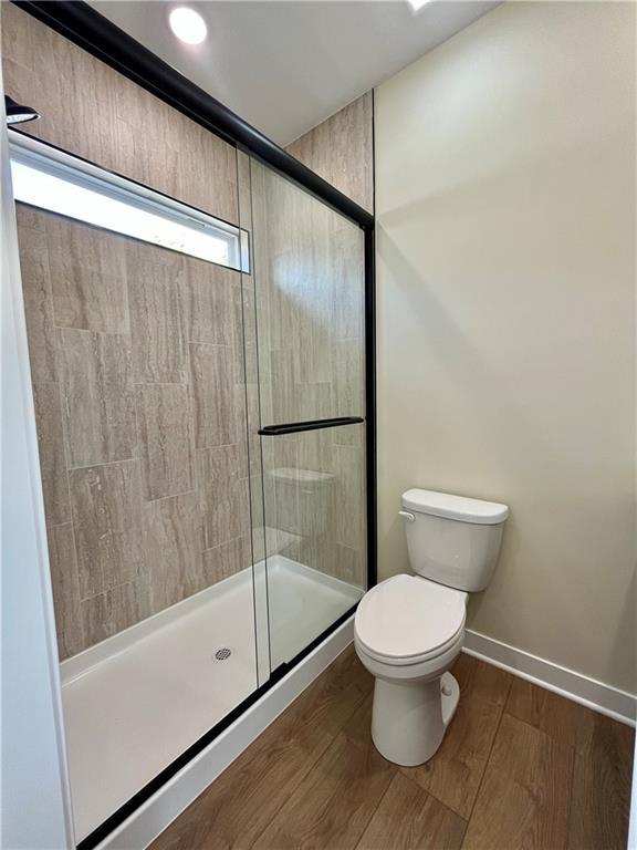 bathroom with a stall shower, toilet, baseboards, and wood finished floors
