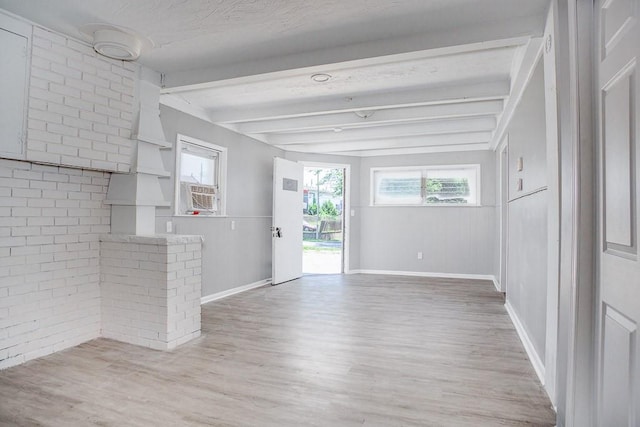 interior space with light wood-style floors, brick wall, baseboards, and beam ceiling