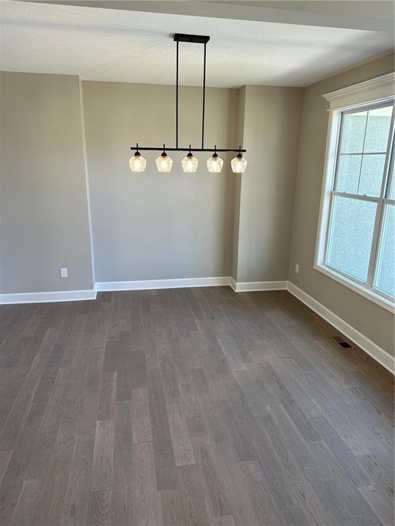 unfurnished dining area with visible vents, dark wood finished floors, and baseboards