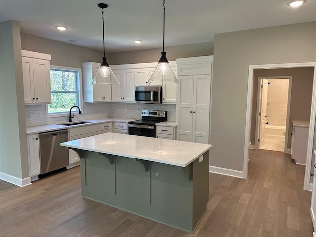 kitchen featuring white cabinets, appliances with stainless steel finishes, a center island, light countertops, and a sink