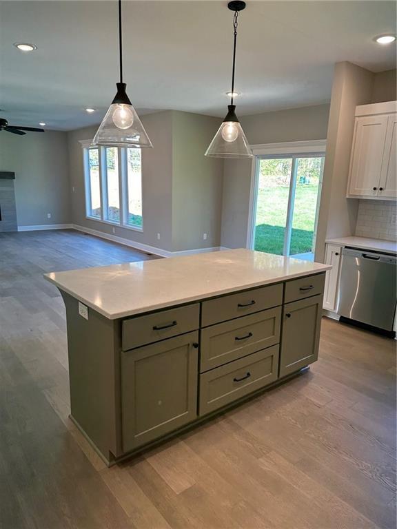 kitchen featuring open floor plan, light countertops, stainless steel dishwasher, and hanging light fixtures