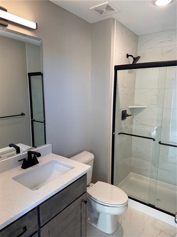 bathroom with toilet, vanity, visible vents, marble finish floor, and a shower stall