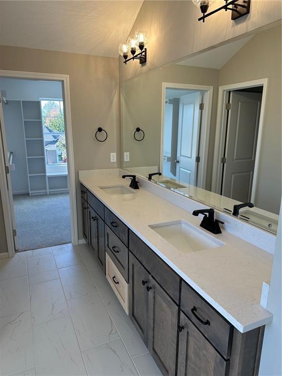 full bath featuring vaulted ceiling, marble finish floor, double vanity, and a sink