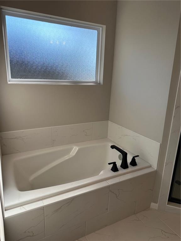 full bathroom featuring marble finish floor and a garden tub