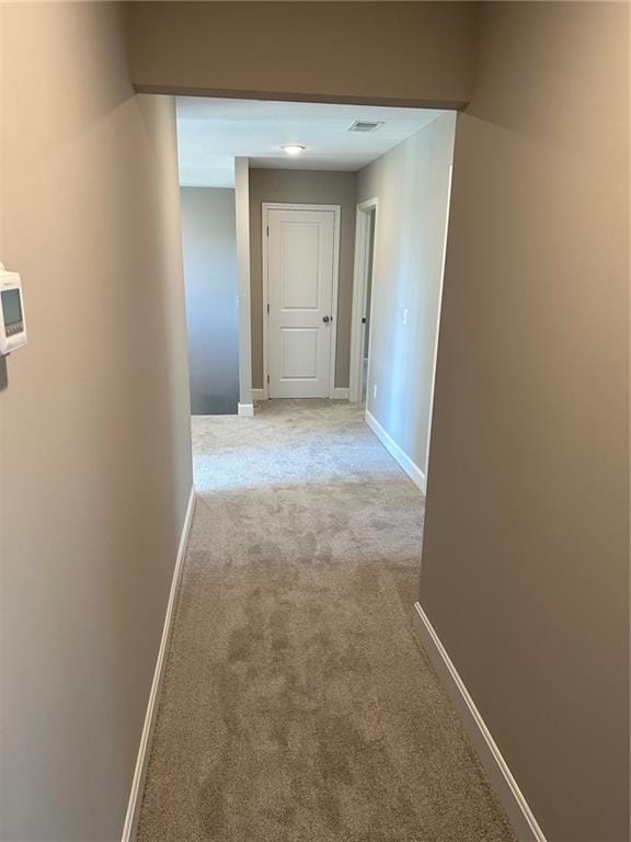 hall with light carpet, visible vents, and baseboards