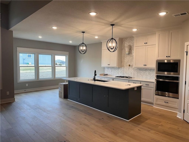 kitchen featuring appliances with stainless steel finishes, white cabinetry, sink, hanging light fixtures, and a center island with sink