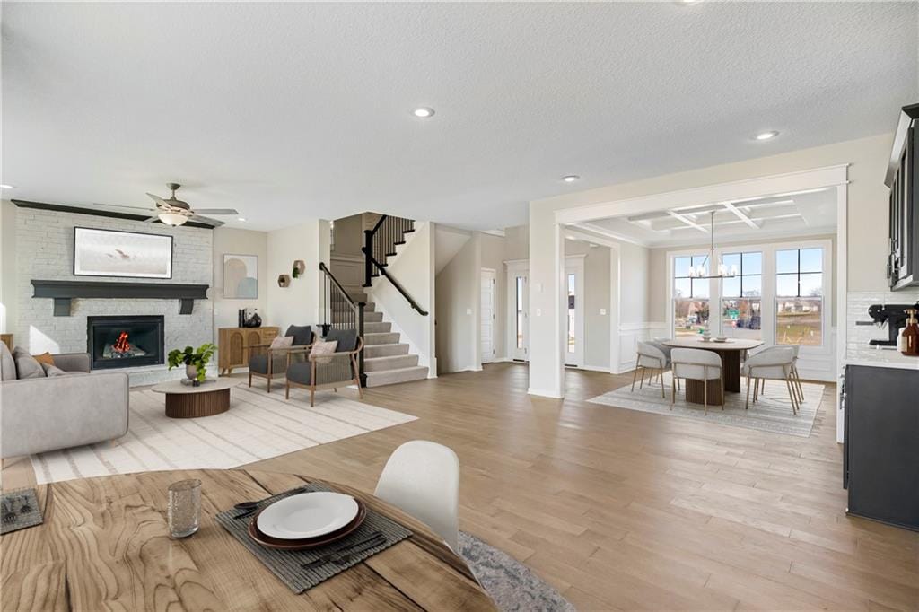 9276 Zarda Dr, Lenexa, KS 66227 - living area featuring stairs, ceiling fan with notable chandelier, a textured ceiling, light wood-style floors, and a brick fireplace