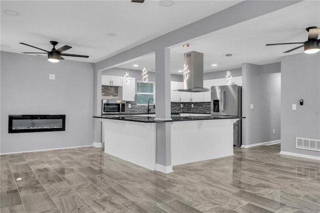 kitchen with ceiling fan, island range hood, a kitchen island, and white cabinets