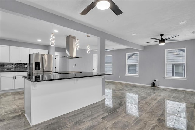 kitchen with tasteful backsplash, stainless steel refrigerator with ice dispenser, white cabinets, wall chimney range hood, and ceiling fan