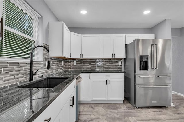 kitchen featuring appliances with stainless steel finishes, backsplash, sink, white cabinets, and dark stone countertops