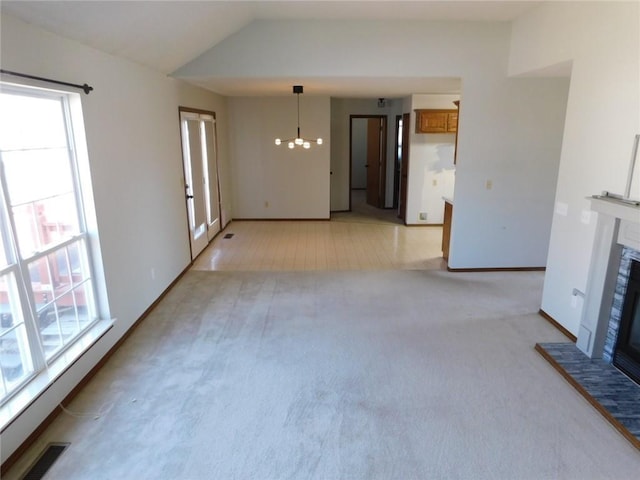 unfurnished living room featuring visible vents, light colored carpet, a fireplace with raised hearth, and vaulted ceiling