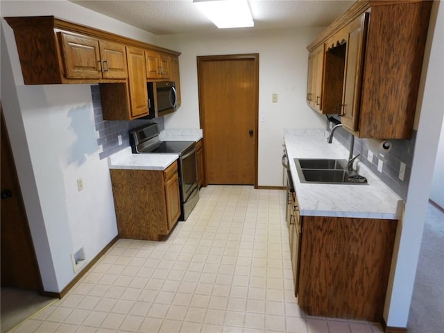 kitchen featuring a sink, appliances with stainless steel finishes, light countertops, decorative backsplash, and baseboards