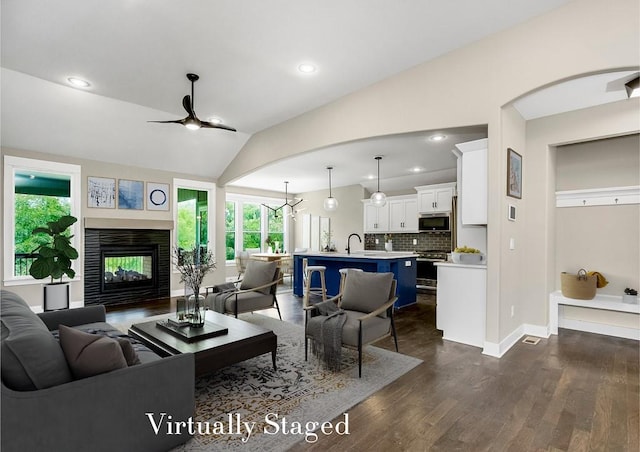 living room featuring a multi sided fireplace, sink, lofted ceiling, dark hardwood / wood-style flooring, and ceiling fan