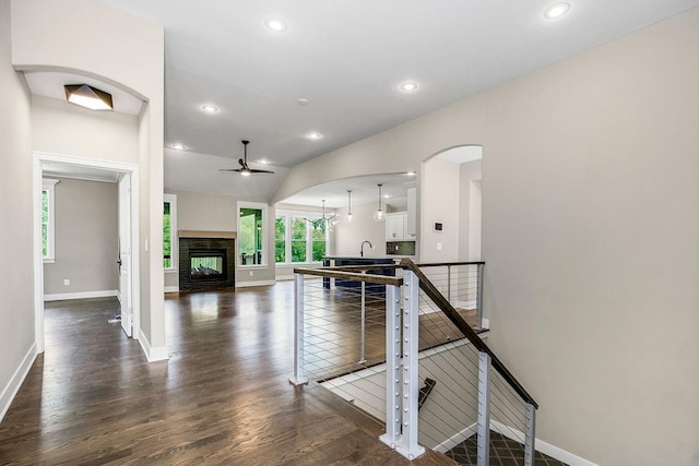 interior space featuring dark hardwood / wood-style flooring, a multi sided fireplace, vaulted ceiling, ceiling fan, and white cabinetry