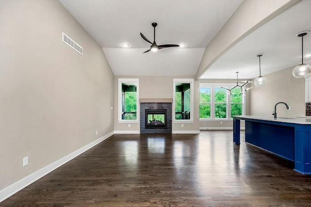 unfurnished living room with sink, dark wood-type flooring, ceiling fan with notable chandelier, a multi sided fireplace, and lofted ceiling