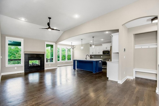 unfurnished living room featuring ceiling fan, a multi sided fireplace, dark wood-type flooring, and lofted ceiling