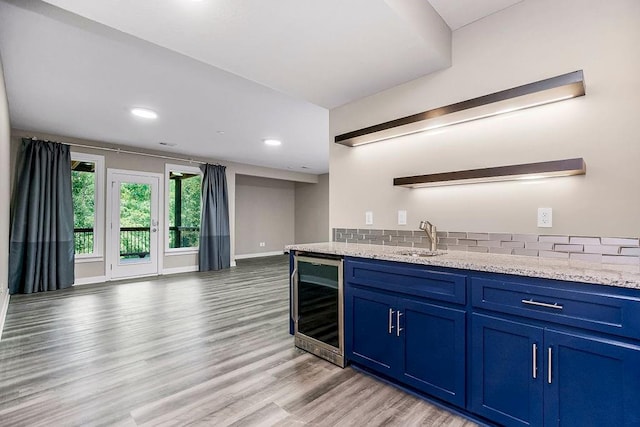 kitchen featuring light hardwood / wood-style flooring, sink, blue cabinetry, wine cooler, and light stone countertops