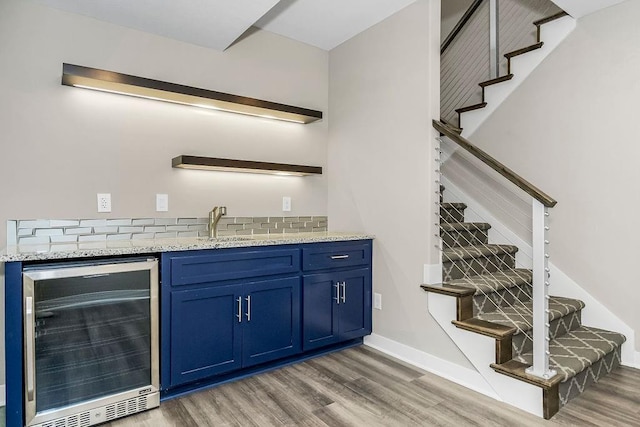 bar featuring tasteful backsplash, beverage cooler, blue cabinetry, light stone countertops, and hardwood / wood-style flooring