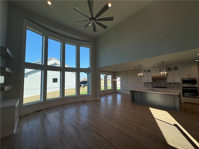 unfurnished living room featuring sink, ceiling fan with notable chandelier, dark hardwood / wood-style floors, and high vaulted ceiling