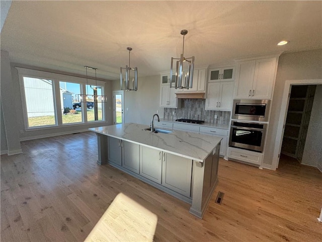 kitchen with white cabinets, a large island with sink, light stone countertops, sink, and stainless steel appliances