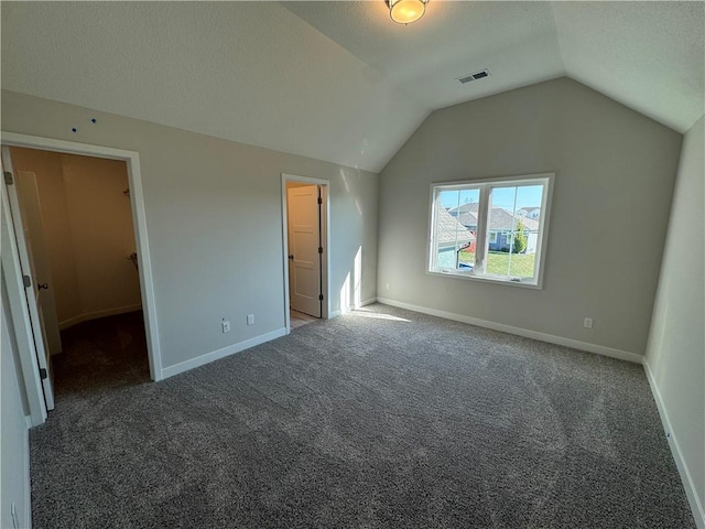 unfurnished bedroom with a closet, dark carpet, ensuite bath, a spacious closet, and vaulted ceiling