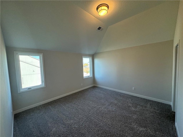 spare room with dark carpet, vaulted ceiling, and a textured ceiling