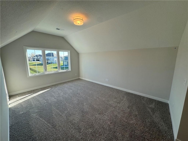 bonus room with a textured ceiling, lofted ceiling, and dark colored carpet