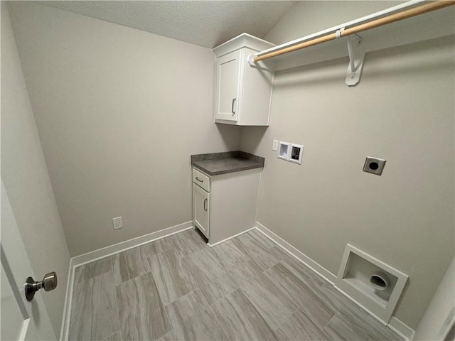 washroom with hookup for an electric dryer, a textured ceiling, washer hookup, and cabinets