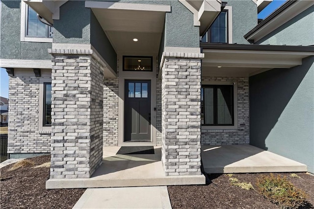 view of exterior entry featuring covered porch, brick siding, and stucco siding