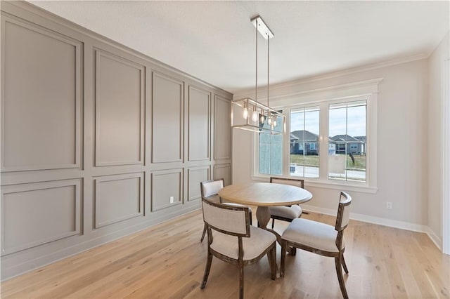 dining space with crown molding, a notable chandelier, a decorative wall, light wood-style flooring, and baseboards