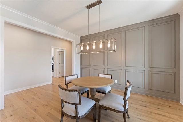 dining room featuring crown molding, light wood-type flooring, a decorative wall, and baseboards