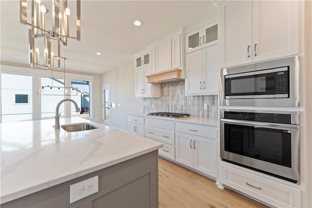 kitchen with tasteful backsplash, white cabinets, appliances with stainless steel finishes, decorative light fixtures, and a sink