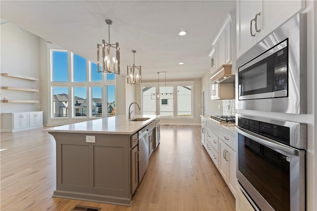 kitchen with appliances with stainless steel finishes, gray cabinets, light countertops, light wood-style floors, and a sink