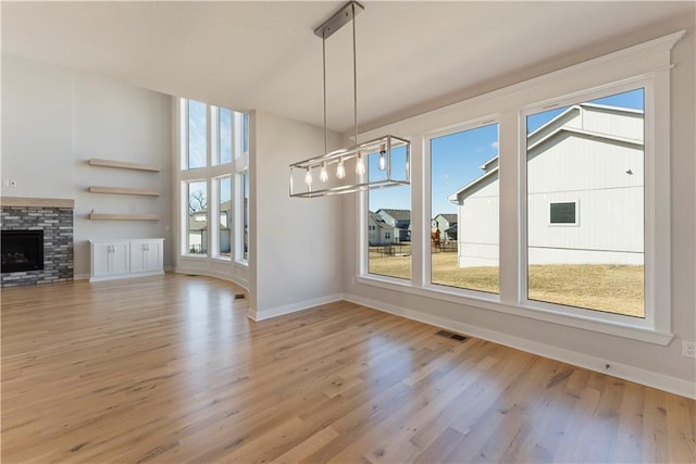 unfurnished dining area featuring a stone fireplace, wood finished floors, visible vents, and baseboards