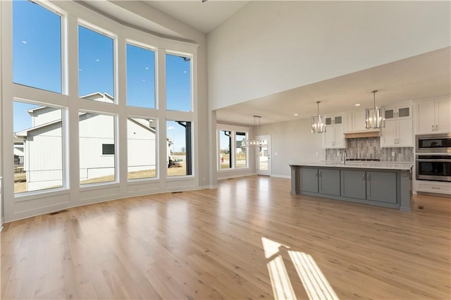 unfurnished living room featuring a high ceiling, visible vents, baseboards, light wood-style floors, and an inviting chandelier