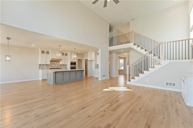 unfurnished living room with baseboards, visible vents, stairway, and light wood finished floors