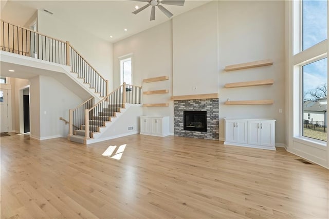 unfurnished living room featuring light wood finished floors, baseboards, a glass covered fireplace, stairs, and a high ceiling