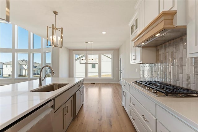 kitchen featuring stainless steel appliances, premium range hood, a sink, tasteful backsplash, and an inviting chandelier