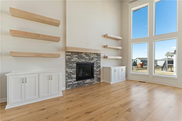 unfurnished living room with light wood finished floors, a brick fireplace, and a high ceiling