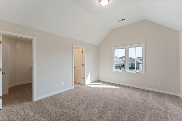 unfurnished bedroom featuring lofted ceiling, light colored carpet, visible vents, baseboards, and a walk in closet