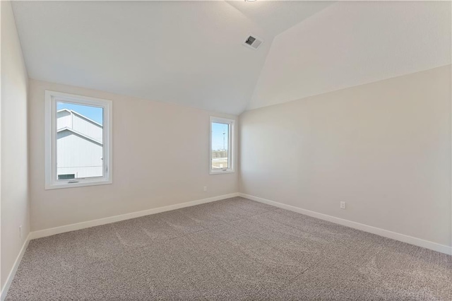 carpeted spare room with lofted ceiling, baseboards, and visible vents