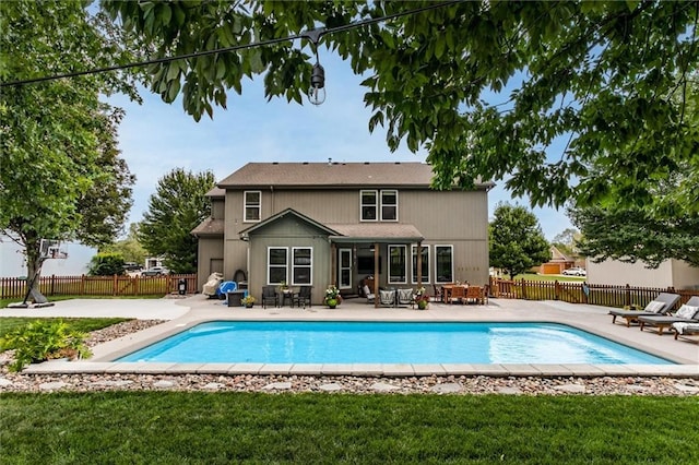 rear view of property featuring a patio area, a lawn, and a fenced in pool